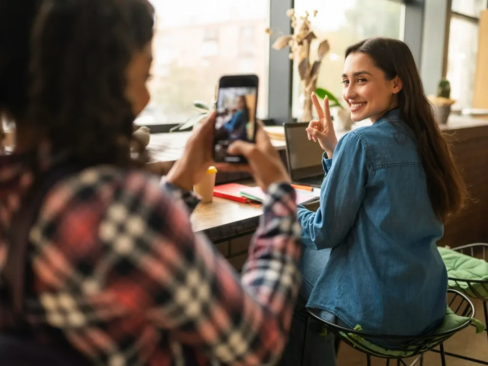 Seorang pelanggan wanita memotret temannya di kafe menggunakan smartphone, ilustrasi nyata dari penerapan strategi User-Generated Content (UGC).